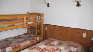 Ein Mehrbettzimmer mit zwei Betten, jedes mit einer karierten Decke. An den Wänden sind Lampen und ein kleiner Nachttisch aus Holz angebracht.