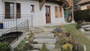 Ein rustikales Chalet mit einer Steintreppe, die zu einer Holztür führt, umgeben von einem Garten mit Steinen und Pflanzen.