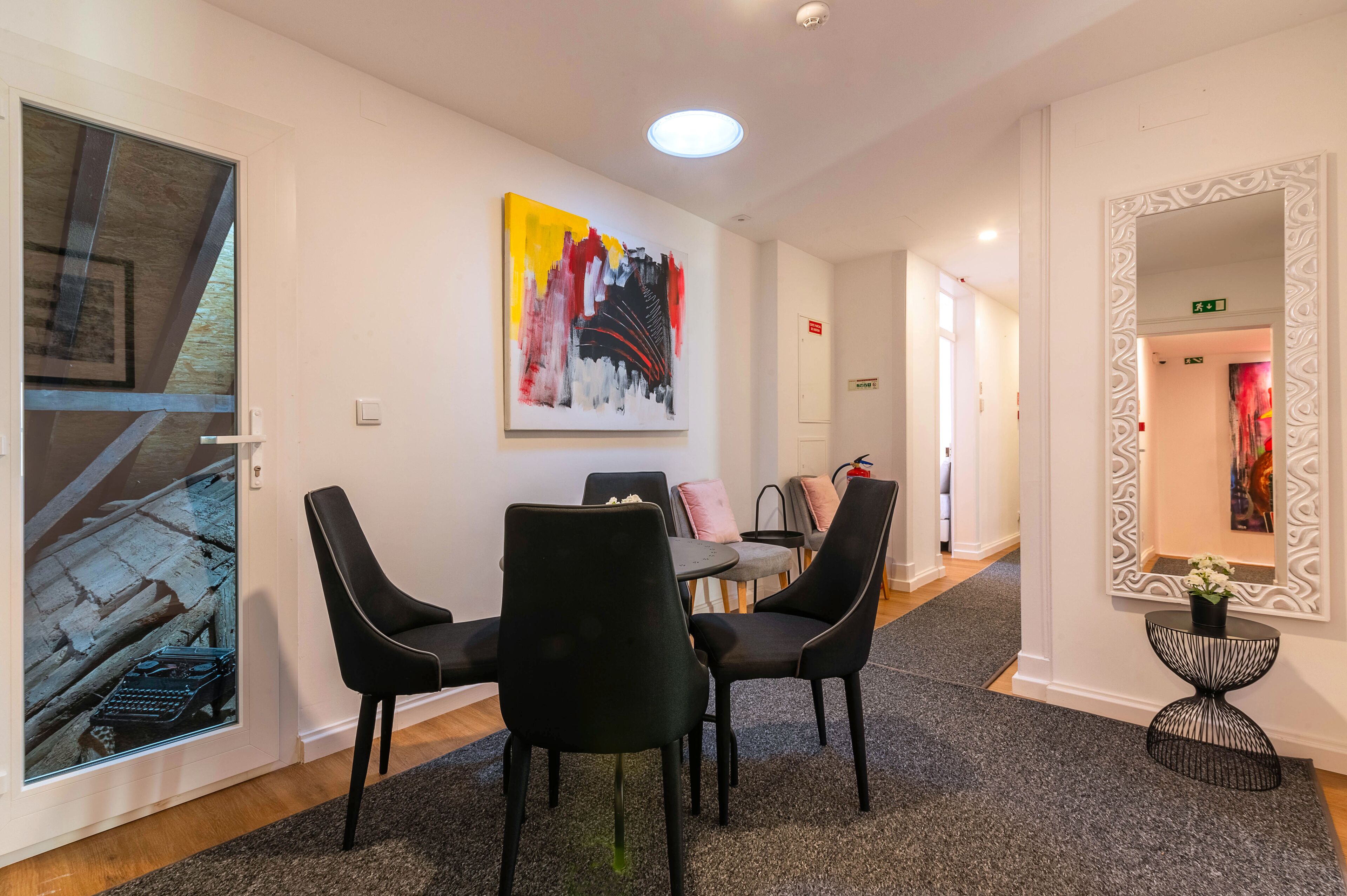 A modern hotel lobby with a dining area featuring black chairs and a table, a large abstract painting on the wall, and a decorative mirror.