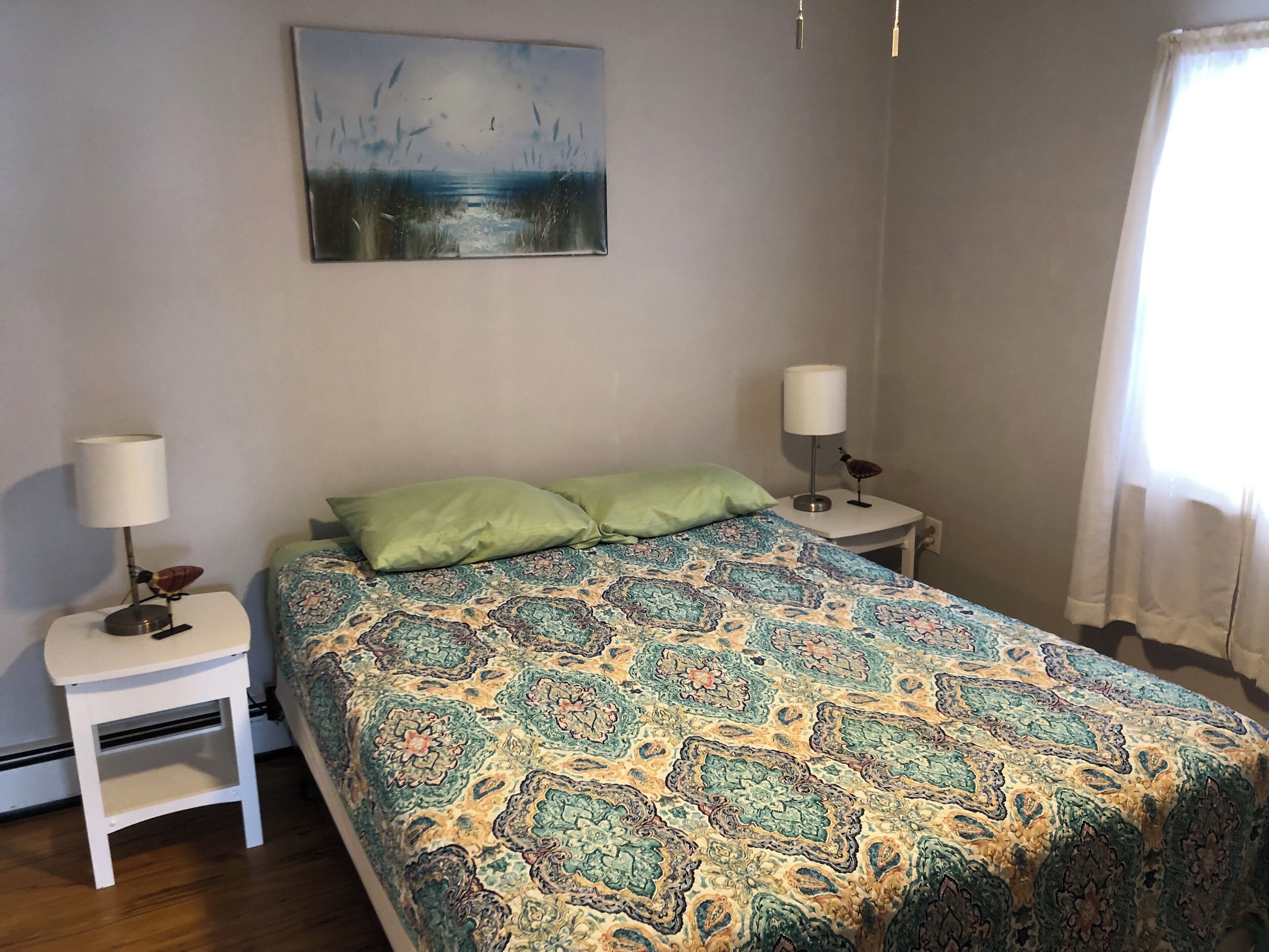 Ein Schlafzimmer mit einem gemusterten Bett, zwei Nachttischen mit Lampen, einem grünen Kissen und einem Bild an der Wand.