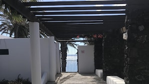 A paved pathway leading to a gated entrance with a pergola overhead. - Top floor apartment with amazing ocean views  (Costa Teguise)