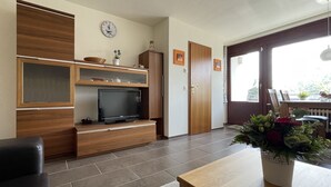 Un soggiorno con una TV su un mobile in legno, un orologio appeso al muro e una porta che dà sull'esterno.