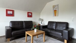 Un soggiorno moderno con due divani in pelle nera, un tavolino in legno e un tappeto decorato. Si vedono due quadri appesi al muro e una lampada su un tavolino.