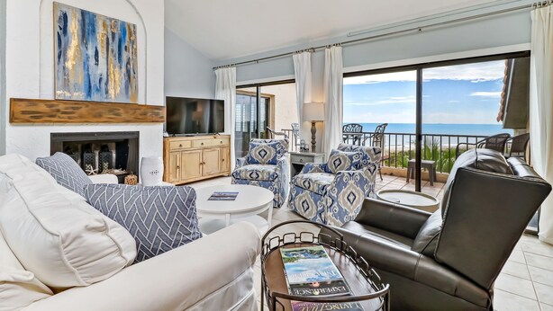 A spacious living room with a fireplace, a large TV, and a balcony with a view of the sea.