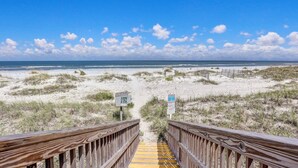 A wooden boardwalk leading to a beach with sand dunes and a clear blue sky.