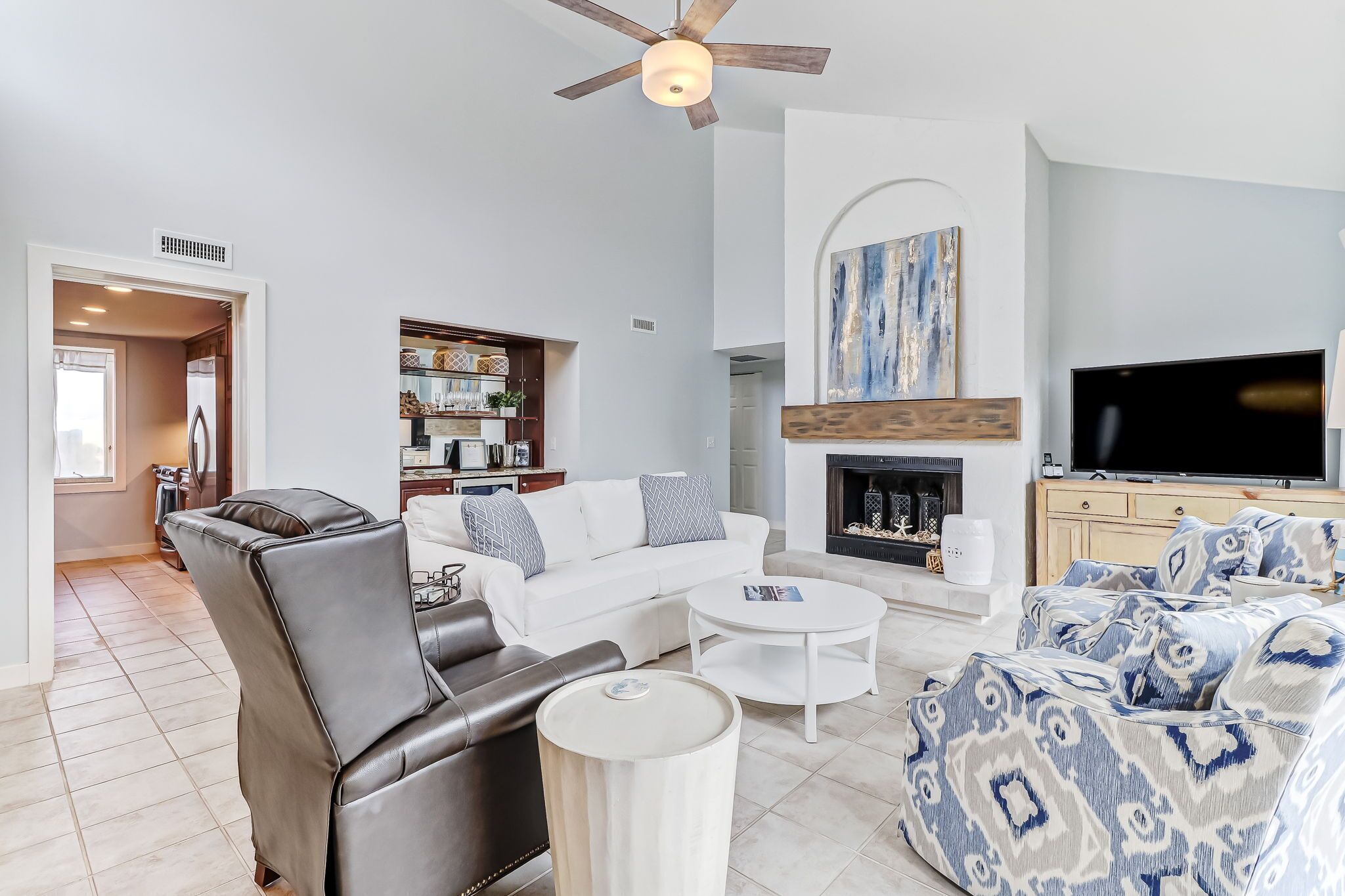 A modern living room with a leather chair, white sofa, patterned ottoman, and a fireplace.