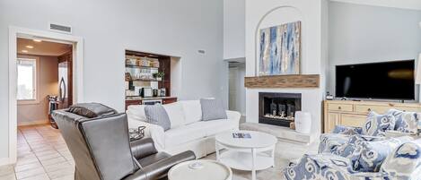 A modern living room with a leather chair, white sofa, patterned ottoman, and a fireplace.
