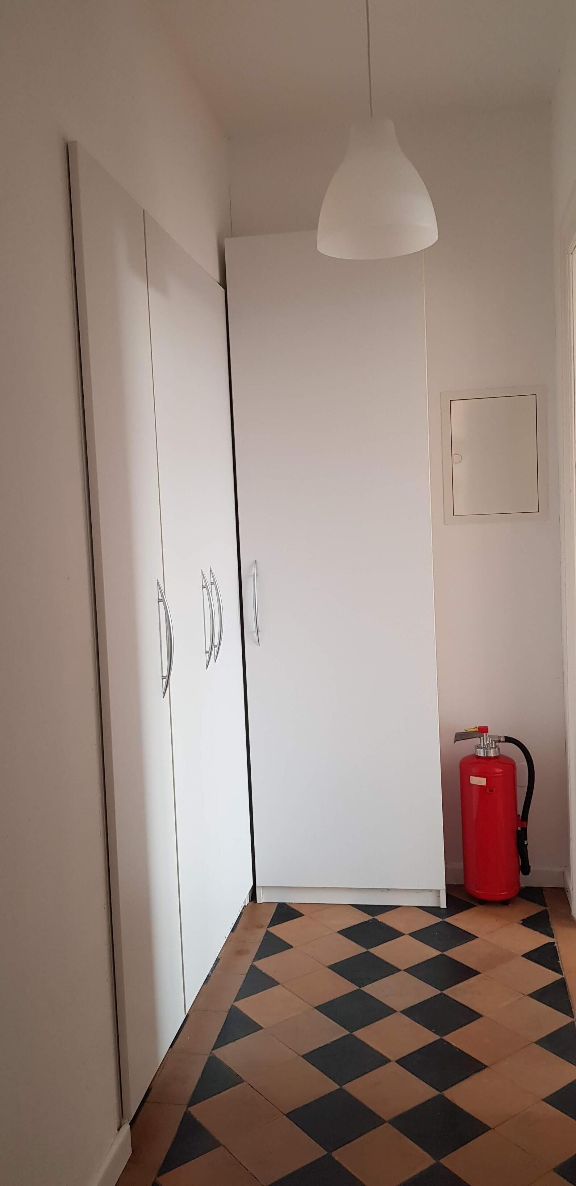 Een kamer met een zwart-wit geruite vloer, een witte garderobe en een rode brandblusser.