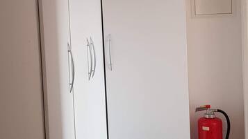 Een kamer met een zwart-wit geruite vloer, een witte garderobe en een rode brandblusser.