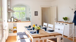 A bright kitchen with a wooden table set for breakfast, a white dining area, and a view of the outdoors through a window. - Hufelandstern - Beautiful old building vacation apartment for up to 7 people with e-charging station (Bad Wildungen)