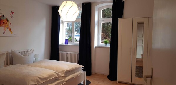 A bedroom with a bed, a radiator, a window with curtains, and a wardrobe.