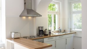 A modern kitchen with white cabinets, a wooden countertop, a built-in stove, a coffee maker, and a window with blinds. - Hufelandstern - Beautiful old building vacation apartment for up to 7 people with e-charging station (Bad Wildungen)