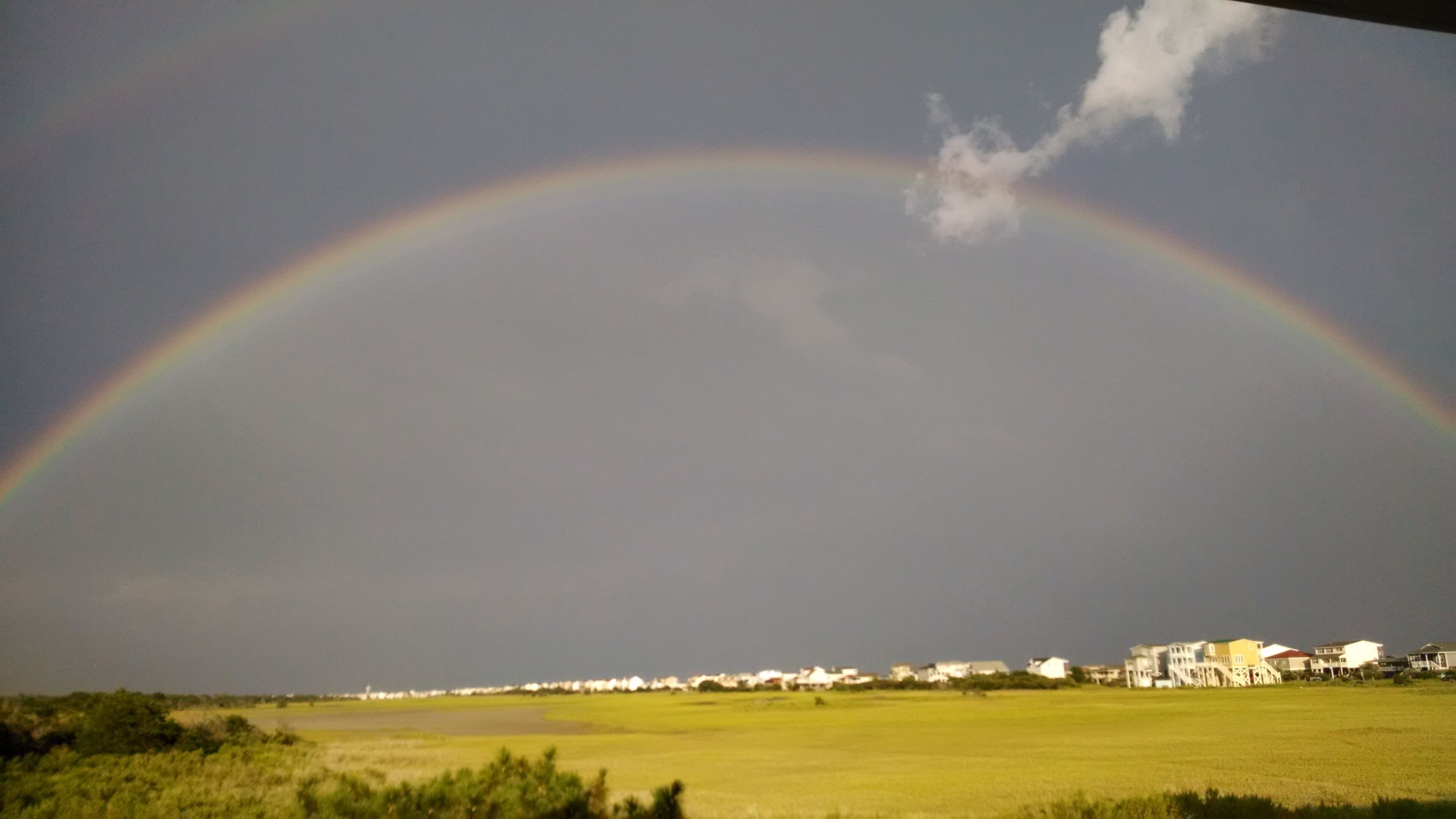 Regnbue over et boligområde med huse i det fjerne.