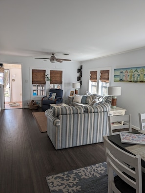 Ein geräumiges Wohnzimmer mit einem großen, gestreiften Sofa, einem Deckenventilator und einem Bild von Strandhütten an der Wand.