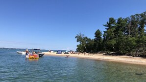 A beach with clear water, a boat, and people on the shore. - Cherry-Pick the Ideal Getaway!  4BR/3BA home @ Traverse City & Torch Lake (Williamsburg)