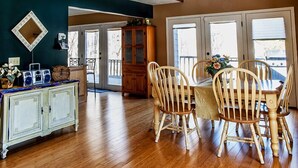 A spacious room with a wooden floor, a dining area with wooden chairs, a cabinet, and a large window. - Cherry-Pick the Ideal Getaway!  4BR/3BA home @ Traverse City & Torch Lake (Williamsburg)