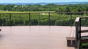 A wooden deck with a metal railing overlooking a vineyard and distant hills. - Cherry-Pick the Ideal Getaway!  4BR/3BA home @ Traverse City & Torch Lake (Williamsburg)