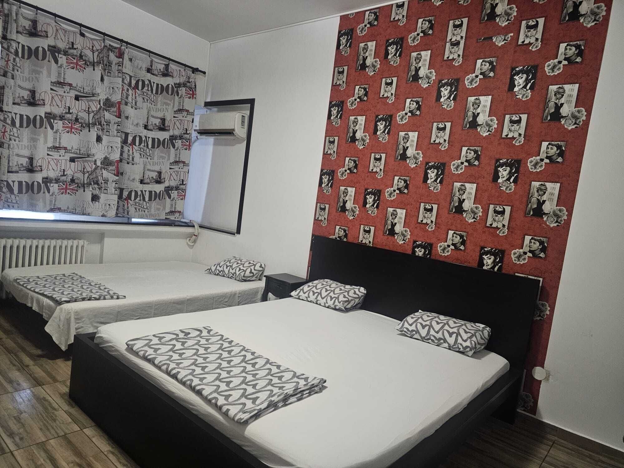 Habitación de hotel con dos camas, pared de diseño rojo y ventana con vistas a edificios.