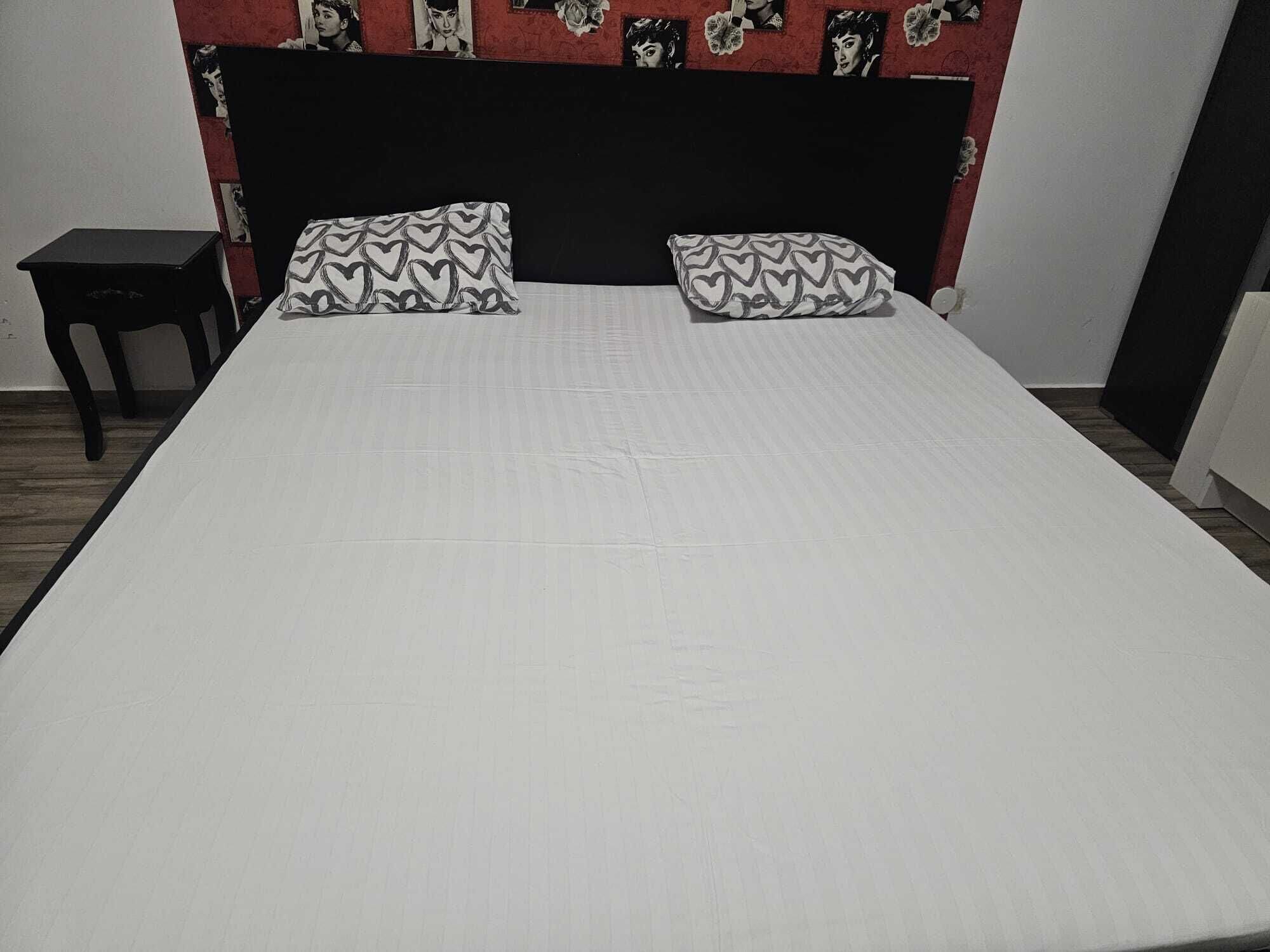 A neatly made bed with a white bedspread and heart-patterned pillows, a black headboard, and a small bedside table.