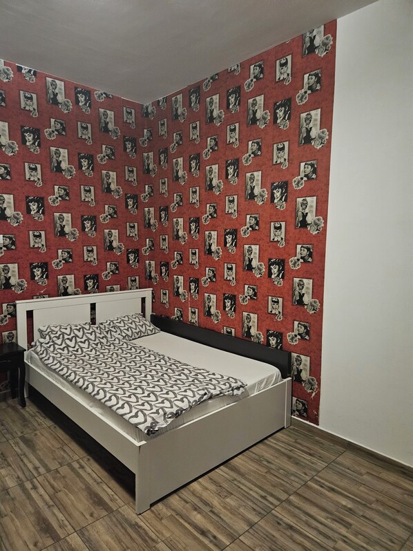 A bedroom with a bed, a nightstand, and a wall covered with patterned wallpaper. - Central Class Bucharest (Bucharest)