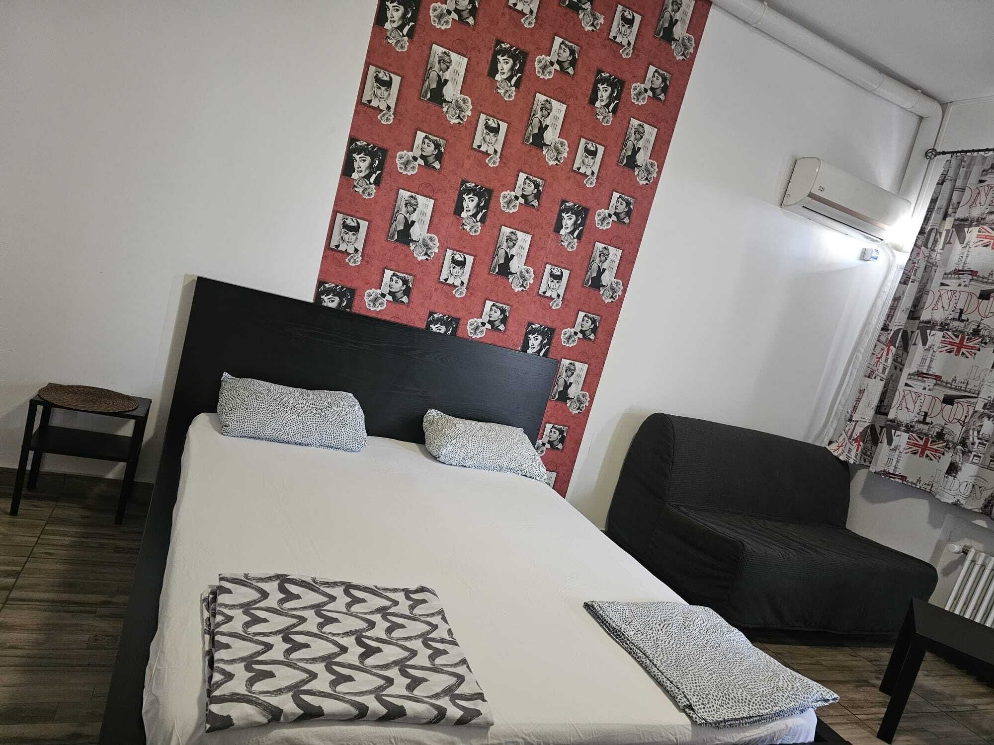 Une chambre à coucher comprenant un lit, une chaise, une petite table et un mur recouvert d’un papier peint à motifs.