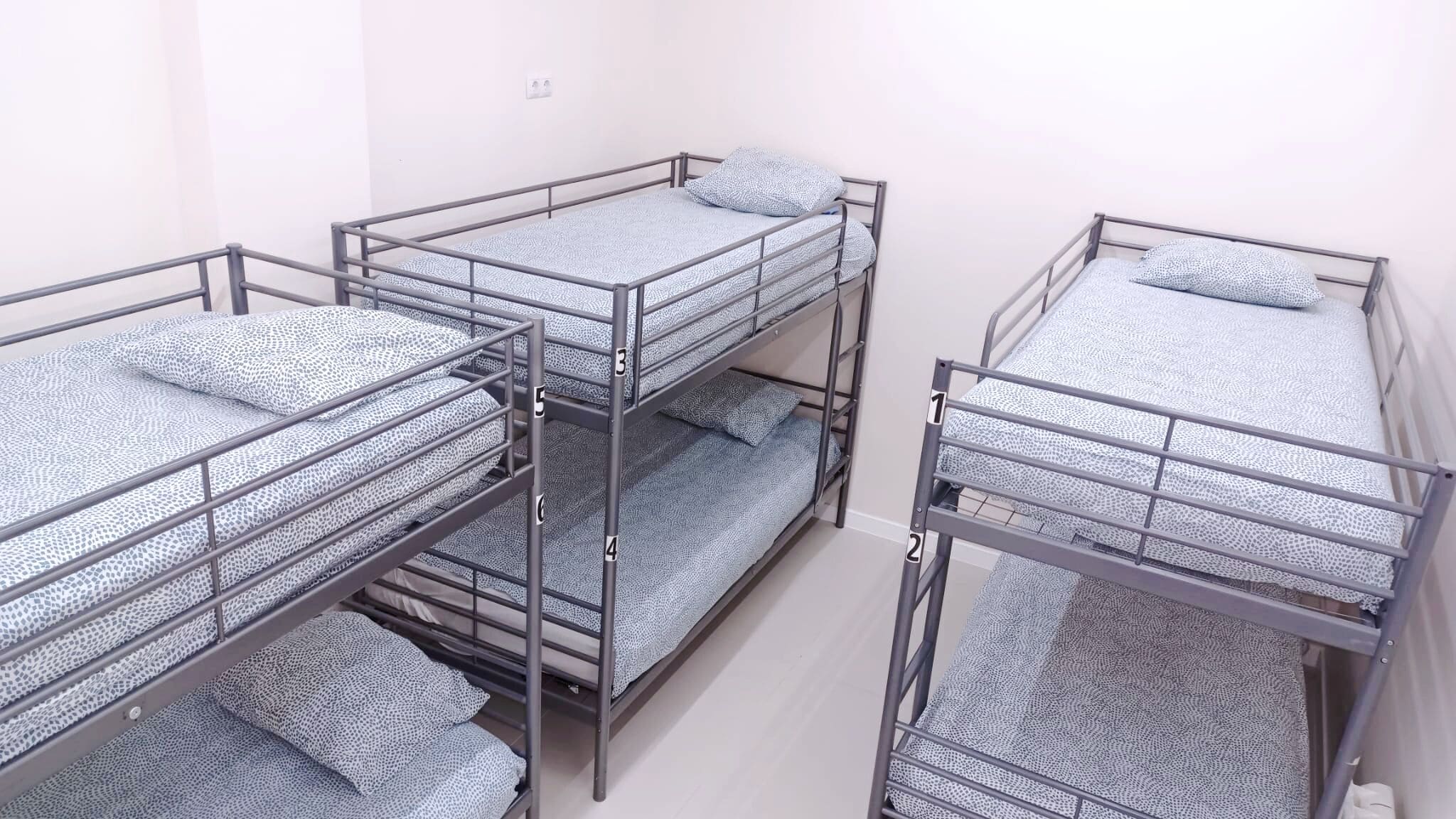 Four bunk beds with metal railings and patterned bedding in a room with white walls.