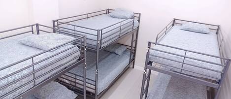 Four bunk beds with metal railings and patterned bedding in a room with white walls.