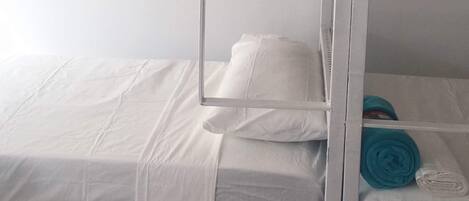 A bunk bed with white bedding and a metal ladder.