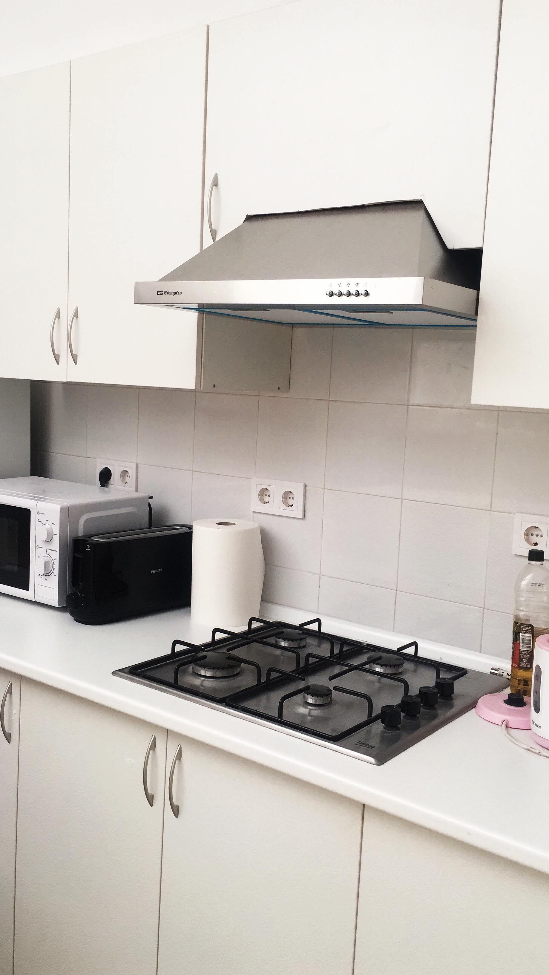 Una cocina con armarios blancos, una estufa a gas, un microondas y un tostador.