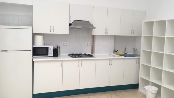 Una cocina compacta con armarios blancos, un microondas, una estufa a gas y un lavamanos.