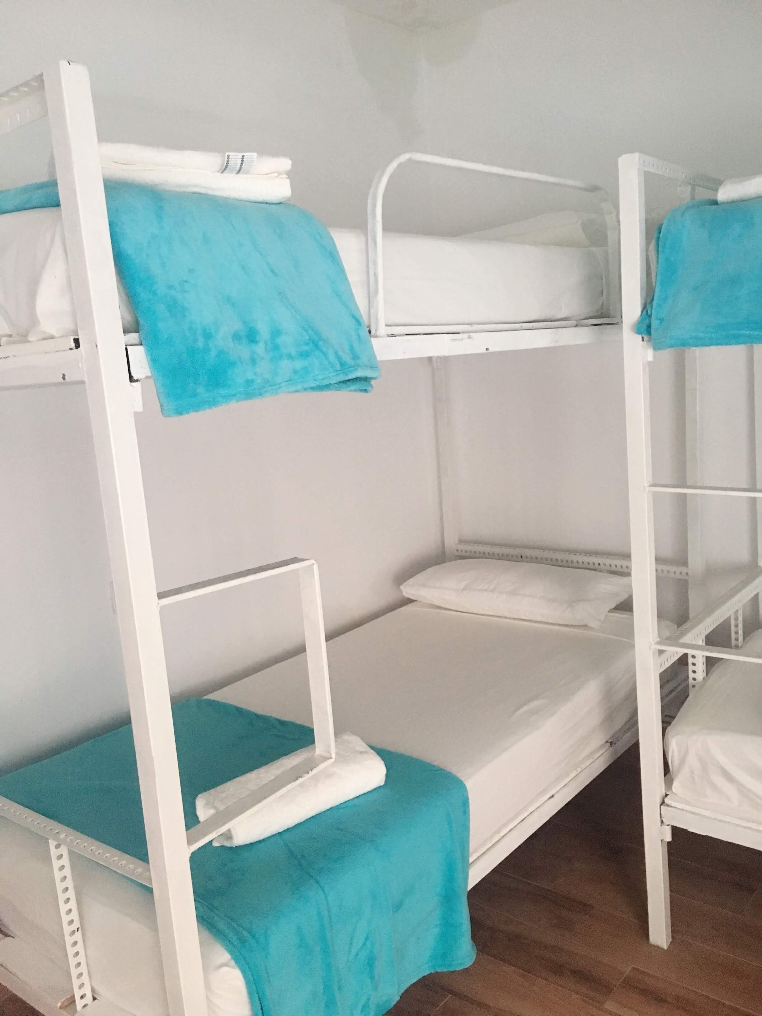 Dormitorio con literas de estructura metálica blanca y ropa de cama color verde azulado.
