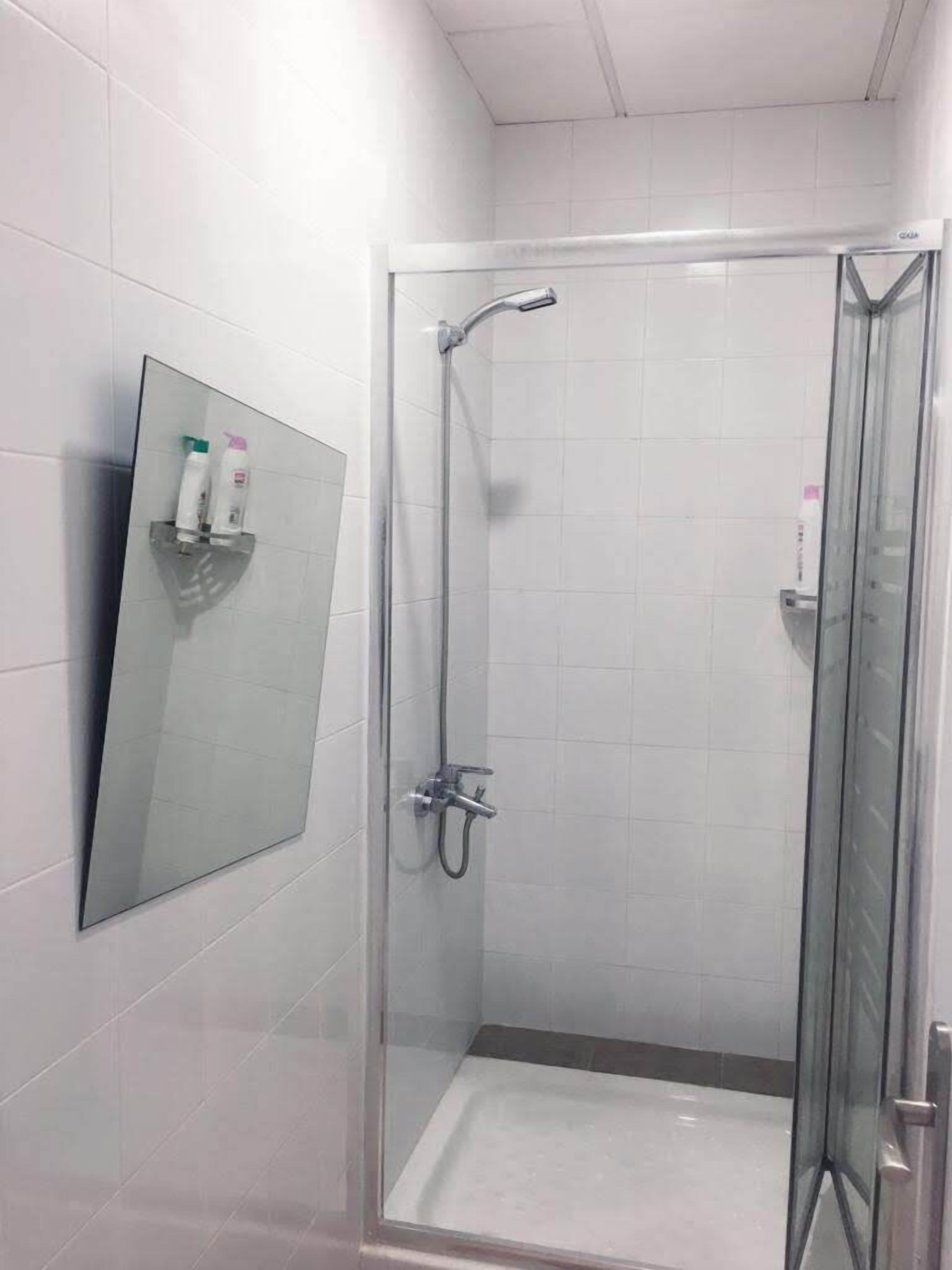 A glass-enclosed shower stall with a handheld showerhead and a wall-mounted faucet.