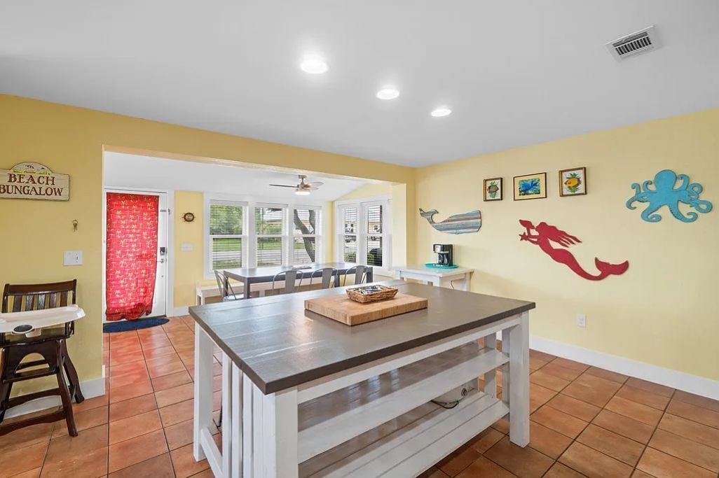 Une cuisine avec un îlot central, un coin repas avec des chaises et un rideau rouge.