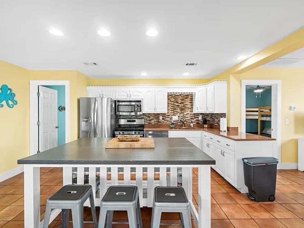 A kitchen with white cabinets, a central island with stools, and a trash bin.