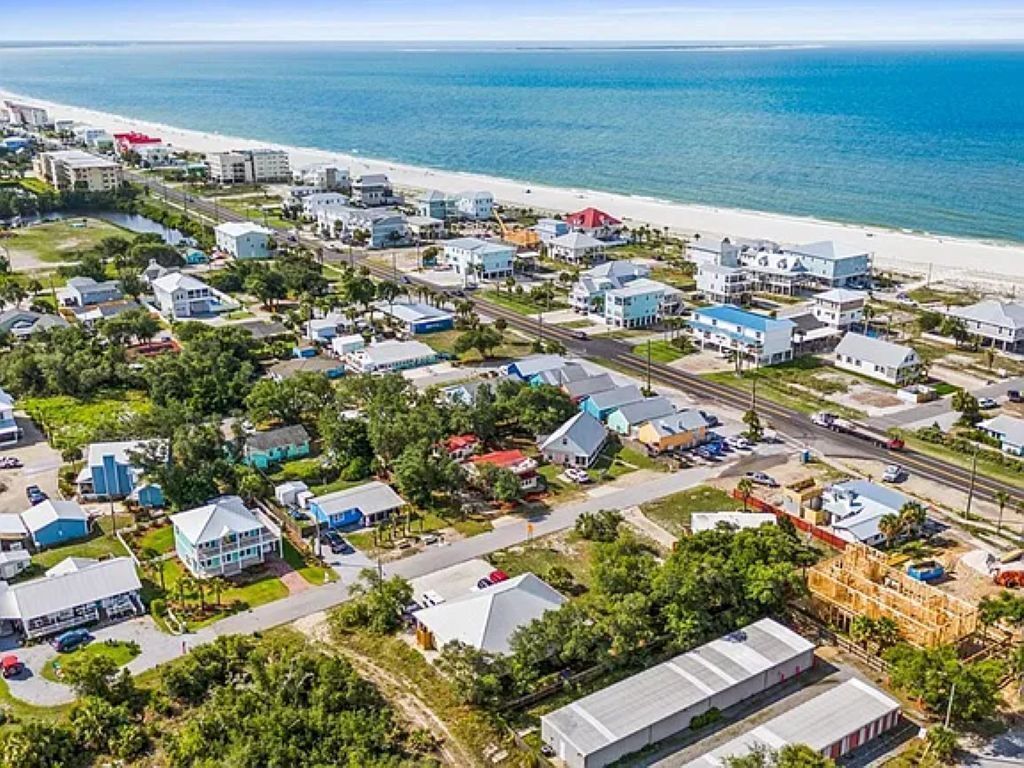 Vue aérienne d’une zone résidentielle côtière, avec des maisons, des routes et une plage.