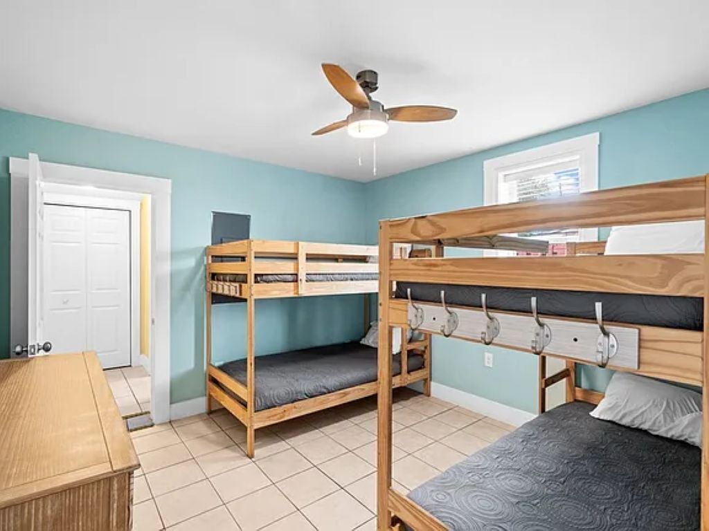 A room with bunk beds, a ceiling fan, a door, and a window.