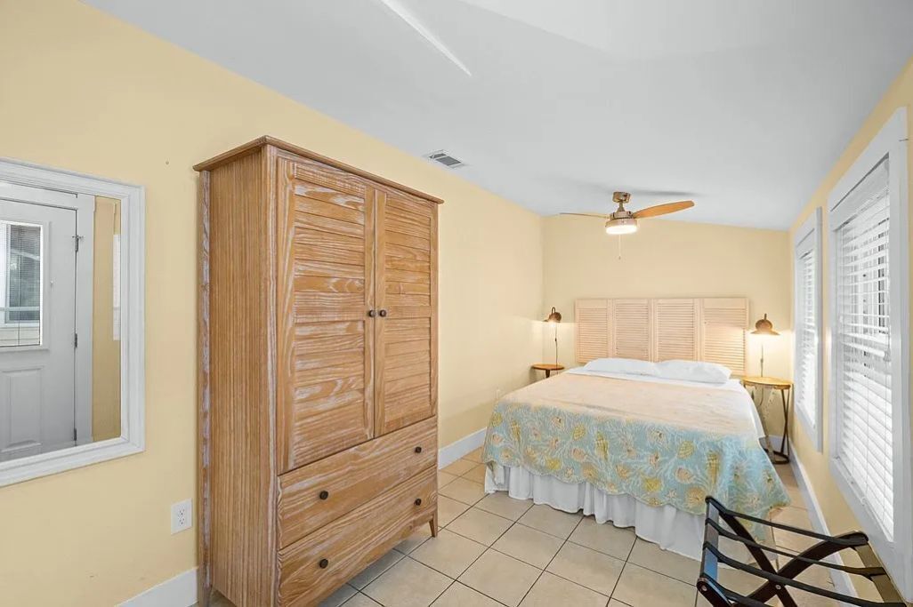 Une chambre avec une armoire en bois, un lit recouvert d’une couvre-lit à motifs floraux, un ventilateur de plafond et deux lampes de chevet.