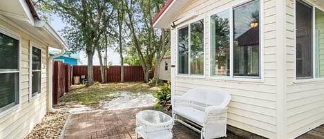 A covered patio with a white wicker chair and a glass table.