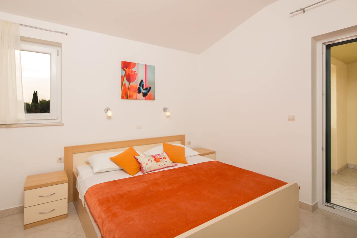 Ein Schlafzimmer mit Bett, Nachttischen, einem Fenster und einer Tür.