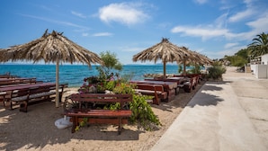 Ein Sitzbereich am Strand mit Holzbänken und Reedsdächern, mit Blick aufs Meer.