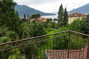 A balcony with a wrought iron railing overlooking a lush garden and a lake with mountains in the background. - Casa Posta 3 in the historic center (Domaso)