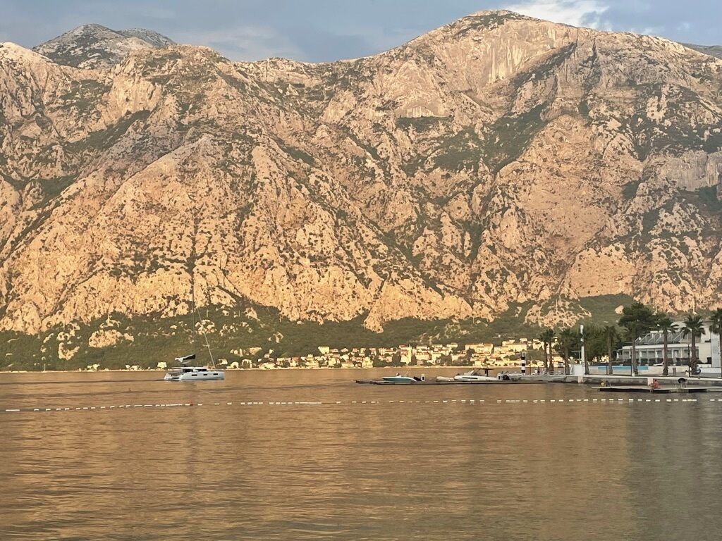 Eine Küstenlandschaft mit Bergen im Hintergrund, Booten, die an der Küste liegen, und einem Yachthafen mit Gebäuden.