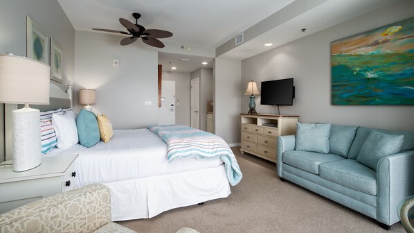 A bedroom with a bed, a ceiling fan, a TV, a painting, and a light-colored carpet. - Gulf View ~ Kitchenette ~ Resort Pool (Miramar Beach)