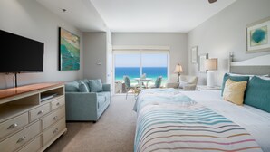 A hotel room with a large bed, a TV, a sofa, and a view of the ocean. - Gulf View ~ Kitchenette ~ Resort Pool (Miramar Beach)