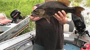 A person holding a fish on a boat with fishing equipment and a calm water body in the background. - fishing and hunting camp (Orr)