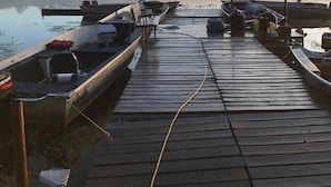 Eine Holzsteganlage mit angebundenen Booten am Ende, ein nebliger See und eine entfernte Baumlinie.