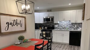 A modern kitchen with white cabinets, a black stove, and a microwave. There's a dining table with a red placemat and black chairs.