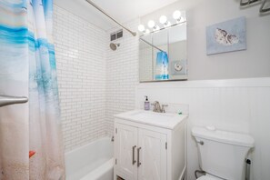 Ein Badezimmer mit einer weißen Badewanne, einem Waschbecken mit Spiegel darüber und einer Toilette. Ein blauer und weißer Duschvorhang ist angebracht.