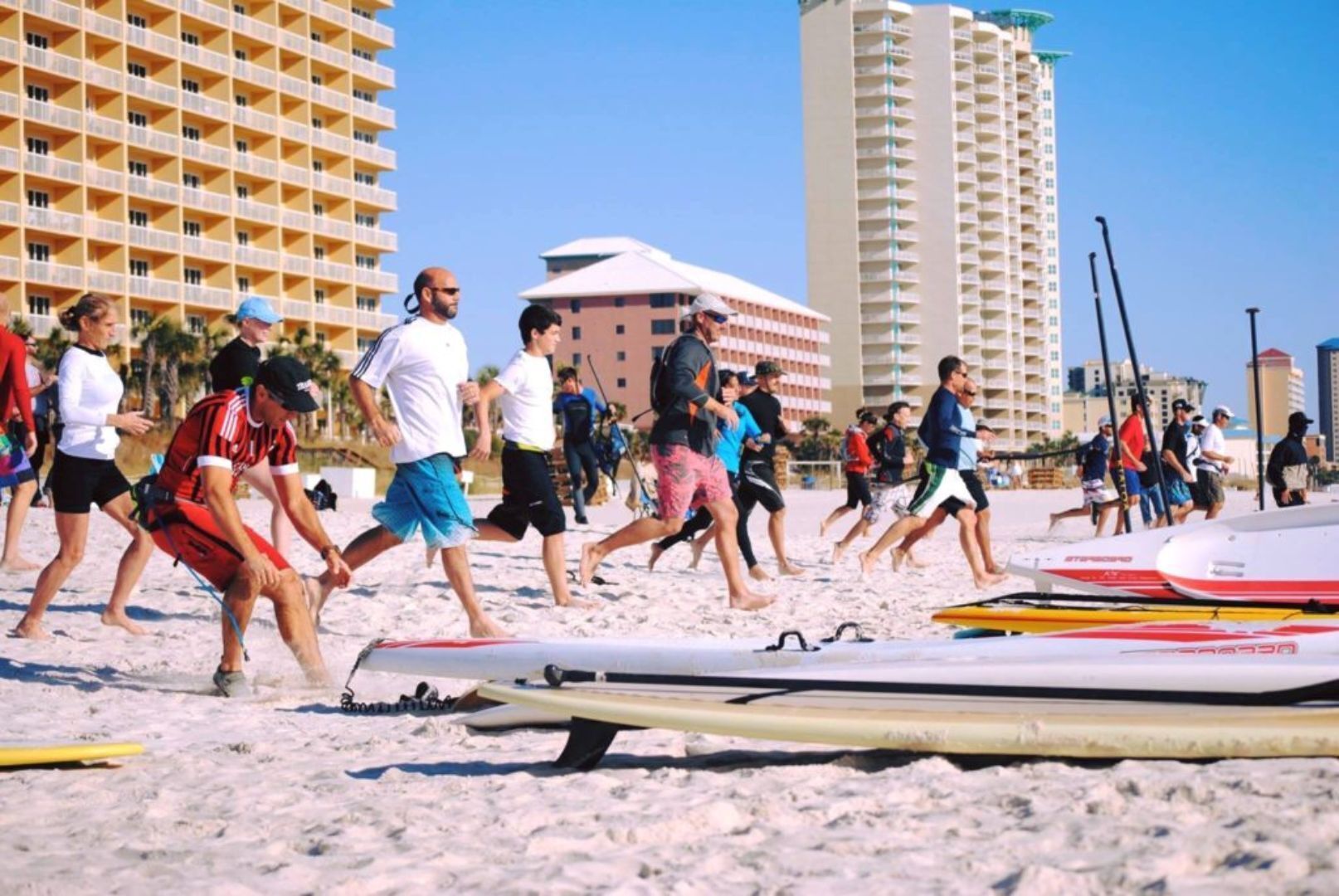 A beach with people running, surfboards, and tall buildings in the background.
