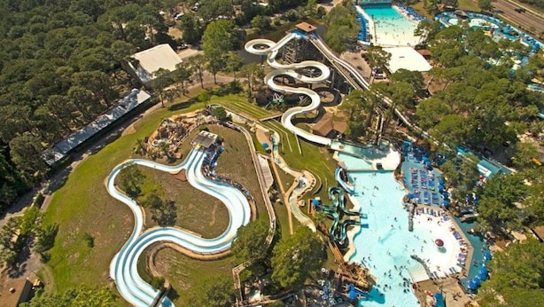 An aerial view of a water park with winding slides, a large pool area, and surrounding greenery.